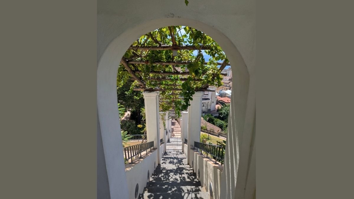 Scalinata bianca con pergolato di viti e vista panoramica sulla città di Salerno e il mare.